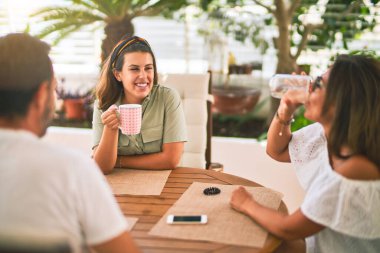 Güzel bir aile terasta oturmuş kahve içiyor, konuşuyor ve gülümsüyor.