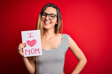 Elinde aşk dolu bir kağıt tutan genç bir kadın anneler gününü mutlu bir yüzle kutluyor. Kendine güvenen bir gülümsemeyle dişlerini gösteriyor.