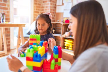 Güzel öğretmen ve küçük kız anaokulunda inşaat bloklarıyla oynuyorlar.