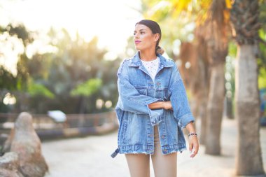 Kot ceket giyen genç ve güzel bir kadın mutlu ve kendinden emin gülümsüyor. Kasaba parkında yüzünde gülümsemeyle dikilirken