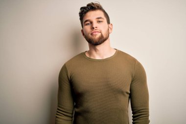 Sakallı, mavi gözlü, beyaz arka planda yeşil süveter giyen genç sarışın adam yüzünde ciddi bir ifadeyle rahatlamış. Basit ve doğal bir şekilde kameraya bakıyorsun..