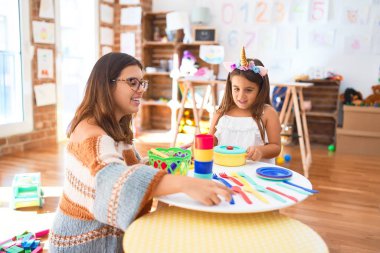 Güzel öğretmen ve çocuk gülümsüyor. Anaokulundaki oyuncakların etrafında plastik yemek ve çatal bıçak kullanarak yemek oynuyorlar.