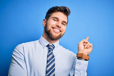 Sarışın, sakallı, mavi gözlü, şık gömlekli ve kravatlı genç bir işadamı yüzünde kocaman bir gülümsemeyle kameraya bakarak elini ve parmağını kaldırıyor..