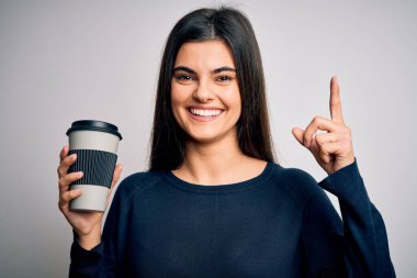 Genç, güzel esmer kadın izole edilmiş beyaz arka planda bir fikir veya soru işareti ile şaşırmış bir fincan kahve içiyor.