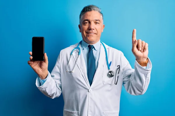 Średni Wiek Przystojny Siwowłosy Lekarz Mężczyzna Trzyma Smartfon Pokazując Ekran — Zdjęcie stockowe