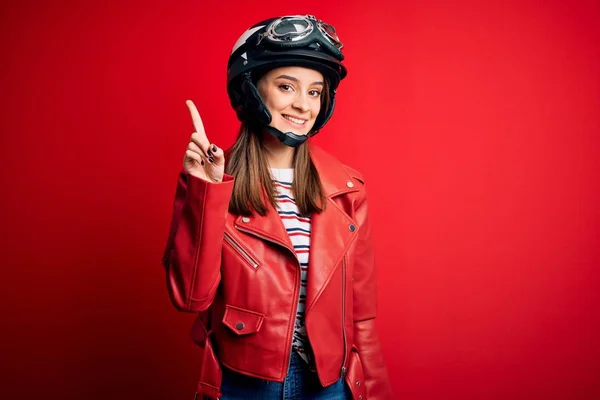 若い美しいブルネットのオートバイのヘルメットと赤いジャケットを身に着けている自転車愛好家の女性が表示され 指の番号1で指摘しながら 自信と幸せ — ストック写真