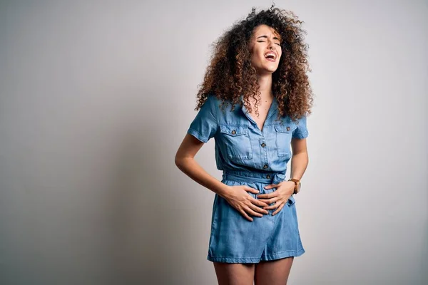 Young beautiful woman with curly hair and piercing wearing casual denim dress with hand on stomach because nausea, painful disease feeling unwell. Ache concept.
