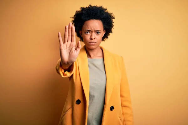 黄色のジャケットを着て巻き毛を持つ若い美しいアフリカ系アメリカ人アフロビジネス女性は 手の手のひらで歌うのをやめます 顔に負と深刻なジェスチャーで警告式 — ストック写真