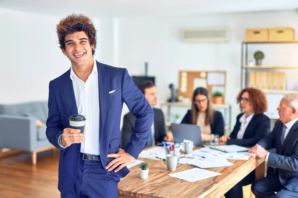 Group of business workers smiling happy and confident working together in a meeting. One of them, standing with smile on face looking at camera drinking coffee at the office.