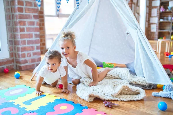 Beautiful toddlers playing inside tipi over blanket around lots of toys at kindergarten