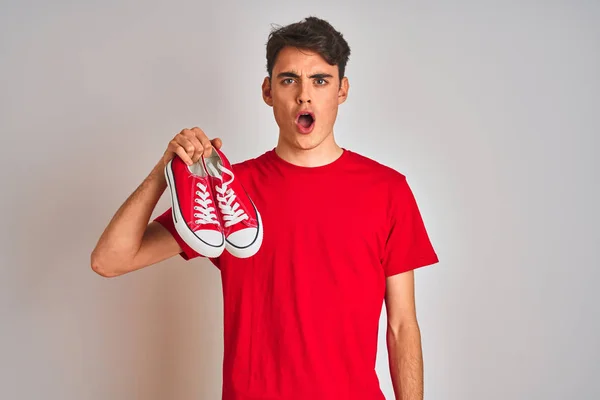 Nastolatek Trzymający Modę Luźne Tenisówki Czerwonym Odizolowanym Tle Przerażony Zaskakującą — Zdjęcie stockowe