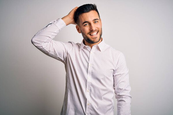 Young handsome man wearing elegant shirt standing over isolated white background smiling confident touching hair with hand up gesture, posing attractive and fashionable