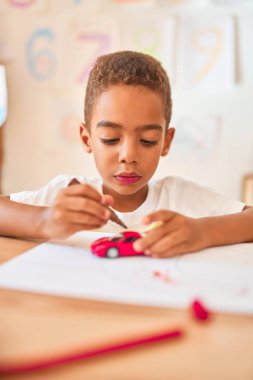 Güzel Afro-Amerikan çocuk. Anaokulunda masa başı kalem kullanarak araba oyuncağı boyuyor.