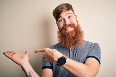 Sakallı ve kolunda dövmesi olan yakışıklı İrlandalı bir adam izole edilmiş arka planda durup kameraya hayret ediyor ve gülümsüyor..