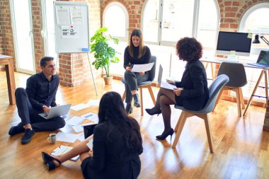 Bir grup iş adamı mutlu ve kendinden emin gülümsüyor. Yüzünde gülümsemeyle yerde rahatça oturmak. Birlikte çalışmak, belgeleri okumak ve ofiste konuşmak.