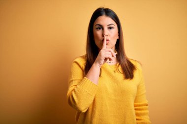 Sarı arka plan üzerine sıradan süveter giyen genç ve güzel bir kadın sessiz olmak istiyor. Sessizlik ve gizli konsept.