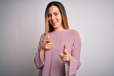 Genç, sarışın, mavi gözlü, dikişli tişört giyen beyaz arka plan üzerinde mutlu ve komik yüzlü parmaklar gösteren bir kadın. İyi enerji ve titreşimler.