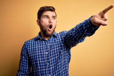 Sarışın, sakallı ve mavi gözlü genç bir işadamı sarı arka planda tişört giyiyor. Parmakla işaret ediyor. İleriyi gösteriyor.