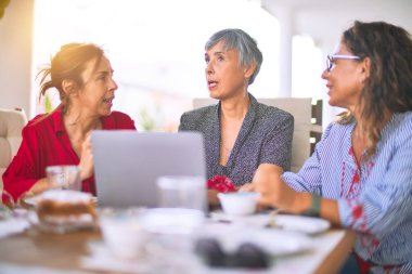 Orta yaşlı kadınlarla buluşup, öğle yemeği yiyip, kahve içiyorlar. Olgun arkadaşlar, güneşli bir günde evde dizüstü bilgisayar kullanarak mutlu bir şekilde gülümserler.