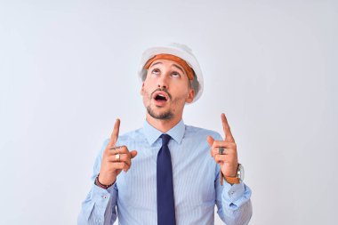 Müteahhit kaskı takan genç bir iş adamı şaşırmış ve şaşırmış bir şekilde yukarı bakıp parmaklarını göstermiş ve kollarını kaldırmıştı..