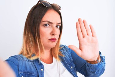 Young beautiful woman wearing denim shirt  standing over isolated white background with open hand doing stop sign with serious and confident expression, defense gesture
