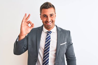 Takım elbiseli ve kravatlı genç yakışıklı iş adamı izole edilmiş arka planda gülümsüyor ve el ve parmaklarıyla 