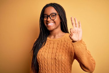 Young african american smart woman wearing glasses and casual sweater over yellow background showing and pointing up with fingers number three while smiling confident and happy.