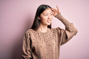 Young beautiful asian woman wearing fashion and elegant sweater over pink solated background smiling confident touching hair with hand up gesture, posing attractive and fashionable