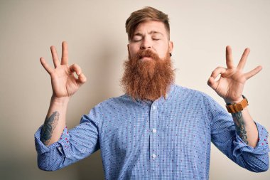 İzole edilmiş arka planda duran, sakallı, yakışıklı, kızıl saçlı iş adamı. Gözleri kapalı, meditasyon yaparken parmaklarıyla gülümsüyor. Yoga konsepti.