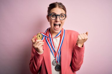 Young beautiful redhead woman wearing medals over isolated red background screaming proud and celebrating victory and success very excited, cheering emotion