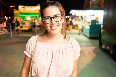 Gözlük takan genç ve güzel bir kadın gecenin ışıklarında mutlu ve heyecanlı bir şekilde gülümsüyor.