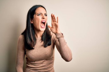 Mavi gözlü genç esmer kadın izole edilmiş beyaz arka plan üzerine günlük süveter giyip el ele tutuşarak bağırıyor ve bağırıyordu. İletişim konsepti.