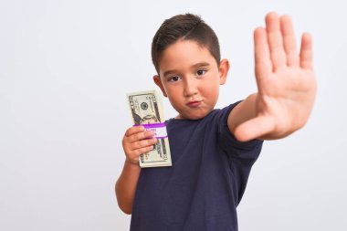Güzel bir çocuk, elinde dolarlarla izole edilmiş beyaz arka planda duruyor. Açık elle dur işareti yapıyor. Ciddi ve kendinden emin bir ifadeyle, savunma hareketi yapıyor.