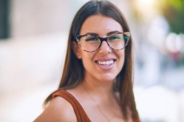 Mutlu ve kendinden emin gülümseyen genç ve güzel bir kadın. Kasaba caddesinde yüzünde gülümsemeyle dikilirken