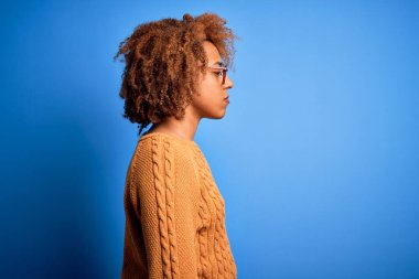 Kıvırcık saçlı, sıradan bir süveter giyen, rahat bir profil pozu veren, kendine güvenen gülümseyen güzel Afro-Amerikan kadın..