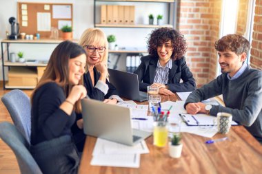 Bir grup iş adamı mutlu ve kendinden emin gülümsüyor. Yüzünde gülümsemeyle çalışmak, dizüstü bilgisayar kullanmak ve ofiste konuşmak.