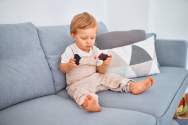Sevimli sarışın çocuk kanepede oturuyor ve evde oynuyor.