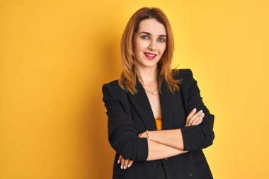 Kızıl saçlı beyaz iş kadını, sarı arka planda izole edilmiş mutlu yüzü kameraya bakarken kollarını çaprazlayarak gülümsüyor. Pozitif kişi.