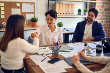 Bir grup iş adamı mutlu ve kendinden emin gülümsüyor. Birlikte çalışırken gülümseyerek ofiste el sıkışırken.