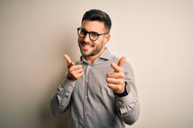 Young handsome man wearing elegant shirt and glasses over isolated white background pointing fingers to camera with happy and funny face. Good energy and vibes.