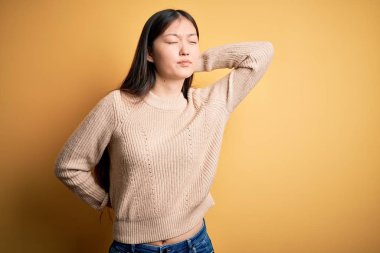 Young beautiful asian woman wearing casual sweater over yellow isolated background Suffering of neck ache injury, touching neck with hand, muscular pain