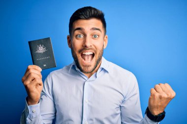 Young handsome tourist man holding australia australian passport id over blue background screaming proud and celebrating victory and success very excited, cheering emotion