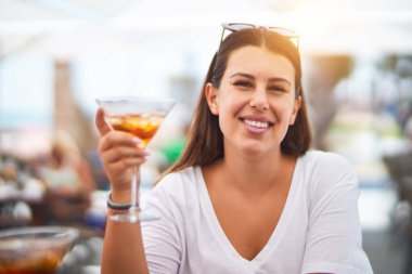 Young beautiful woman sitting at terrace of a restaurant drinking cocktail smiling