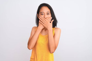 Young chinese woman wearing yellow casual t-shirt standing over isolated white background shocked covering mouth with hands for mistake. Secret concept.