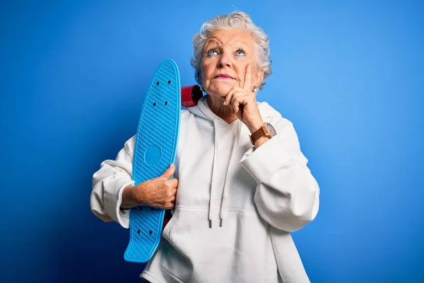 Starsza Piękna Sportowa Kobieta Trzyma Łyżwy Stojąc Nad Odizolowanym Niebieskim — Zdjęcie stockowe