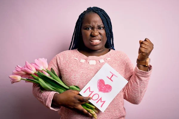 Plus size african american woman holding love mom message and tulips on mothers day annoyed and frustrated shouting with anger, crazy and yelling with raised hand, anger concept