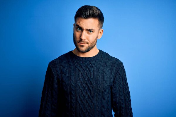 Young handsome man wearing casual sweater standing over isolated blue background skeptic and nervous, frowning upset because of problem. Negative person.