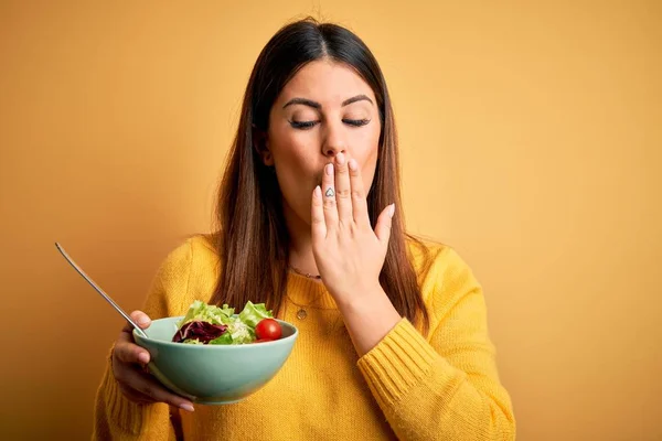年轻美丽的女人吃着健康的新鲜沙拉盖在黄色背景的嘴上 手被错误 恐惧的表情 沉默的恐惧 秘密的概念震惊了 — 图库照片