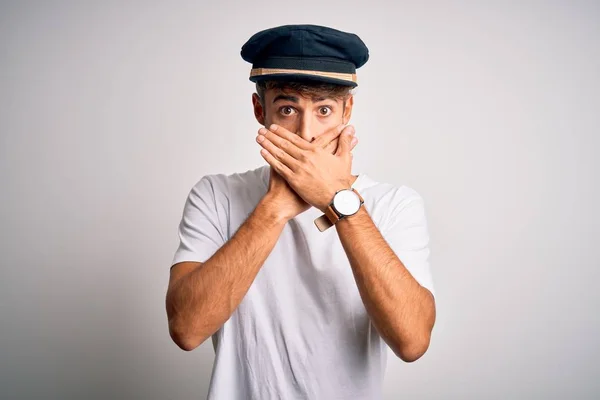 Young driver man with beard wearing hat standing over isolated white background shocked covering mouth with hands for mistake. Secret concept.