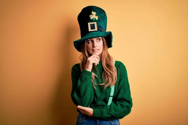 質問について考えて顎に手で聖人の公園の日を祝うクローバーと緑の帽子を身に着けている美しいブルネットの女性 集中的な表現 思慮深い顔で微笑んだ 疑いの概念 — ストック写真